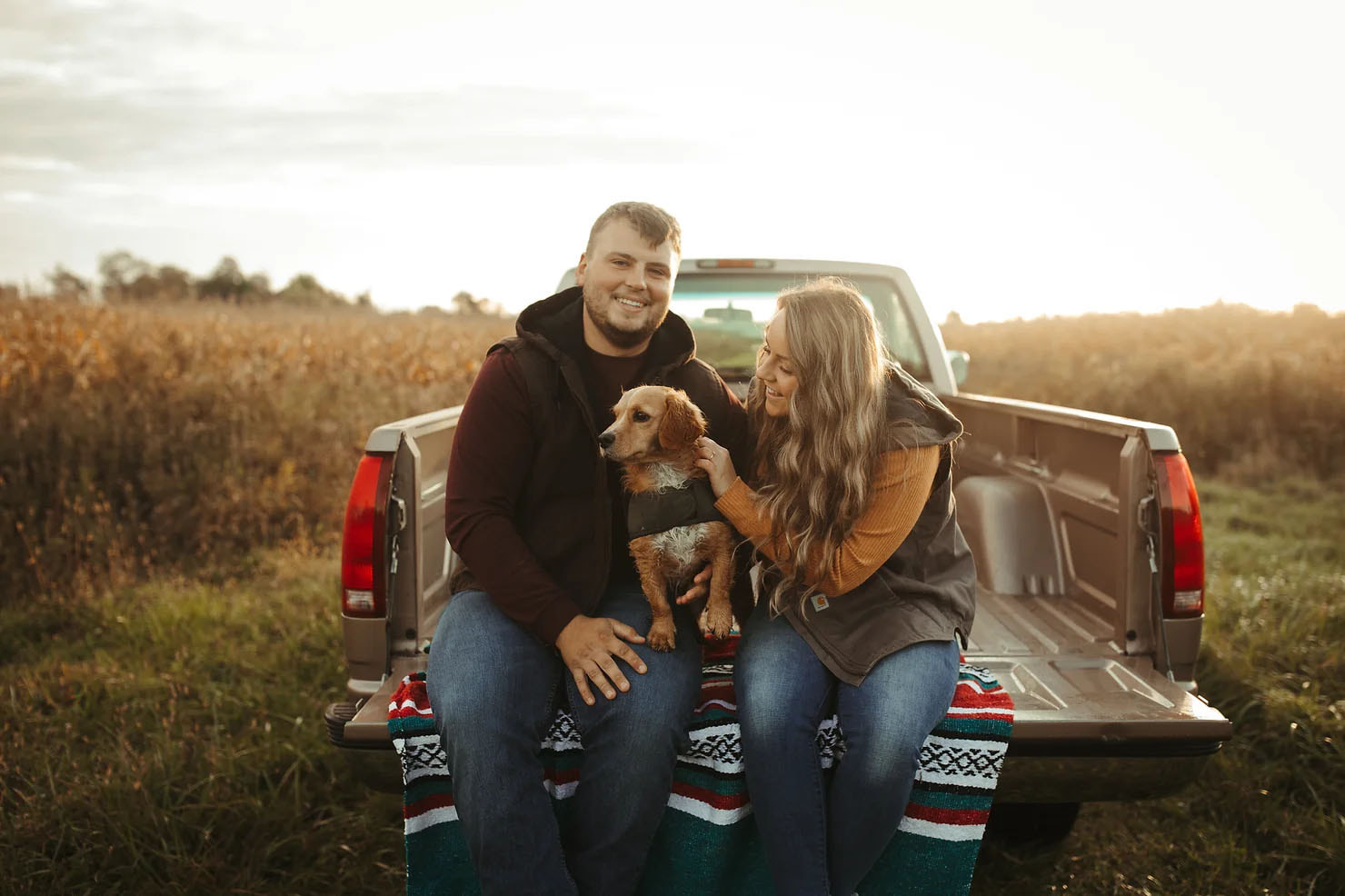 A couple sitting in the back of their pickup truck with their dog for their Michigan engagement photos