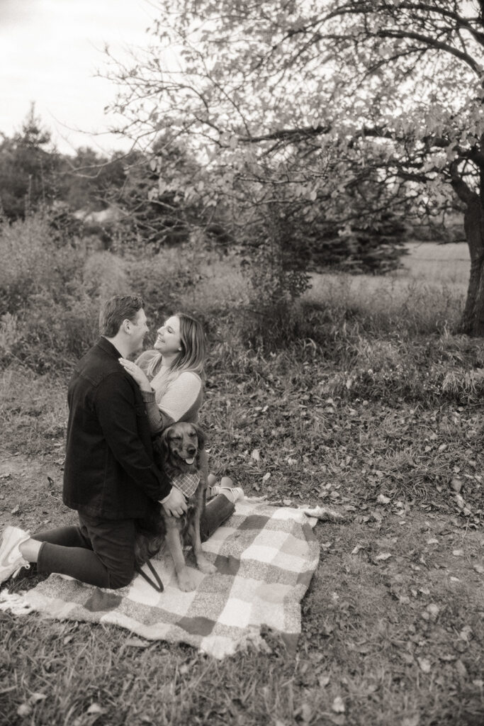 Black and white photo of a couple on a blanket with their dog 