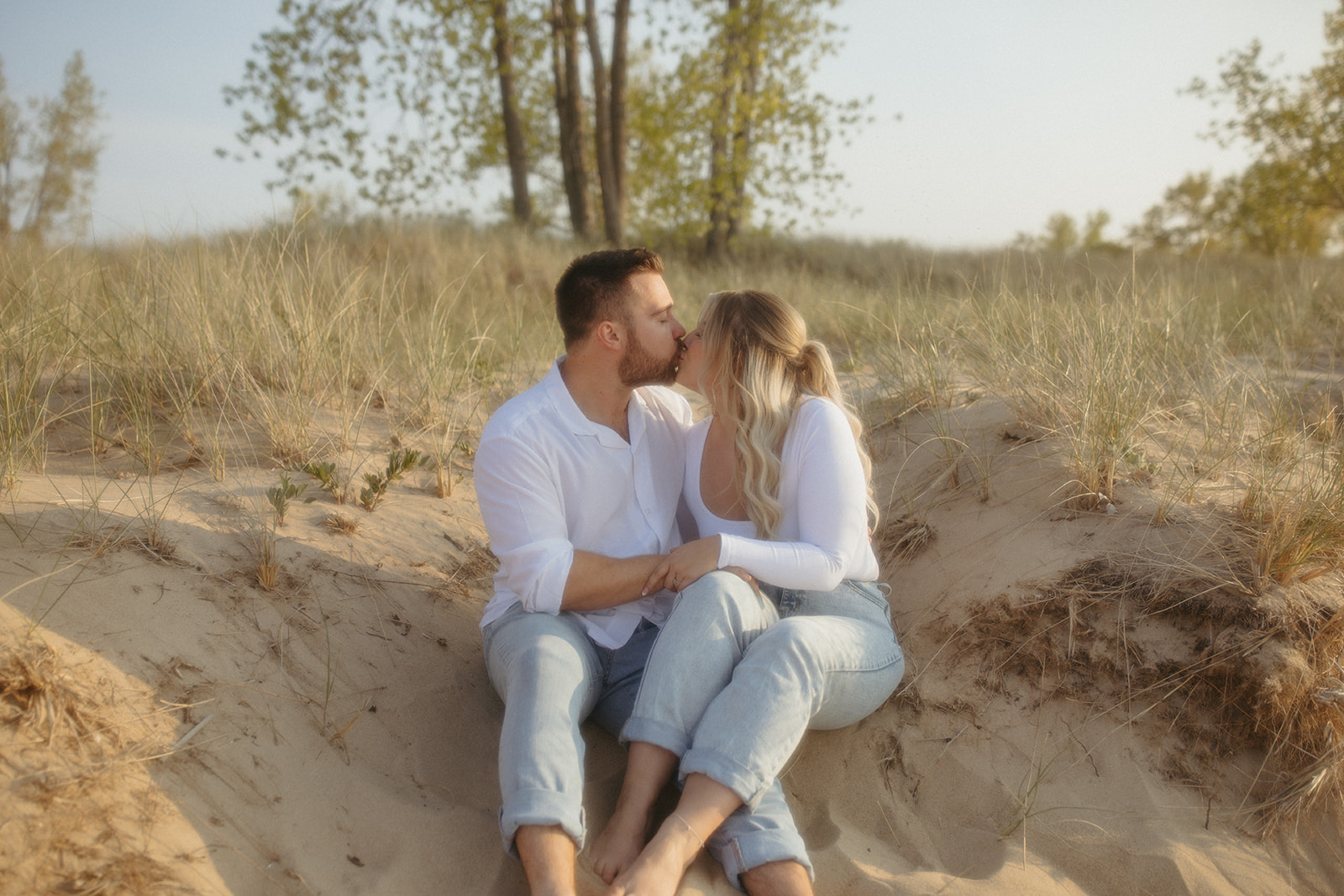 Couple sitting in the sand for their Michigan beach engagement photos at Sleeper State Park