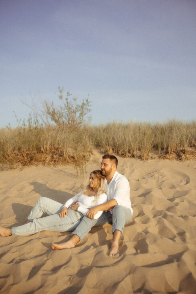 Couple sitting in the sand for their Michigan beach engagement photos at Sleeper State Park