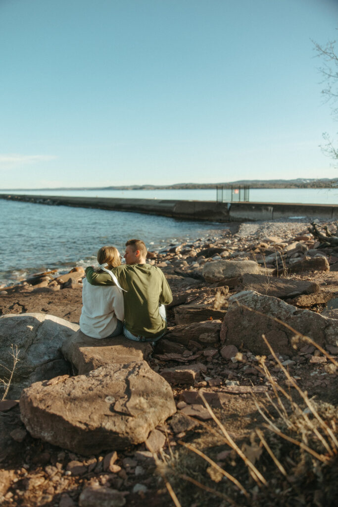 Man and woman sitting on rocks admiring Lake Superior during their Marquette Michigan engagement photos