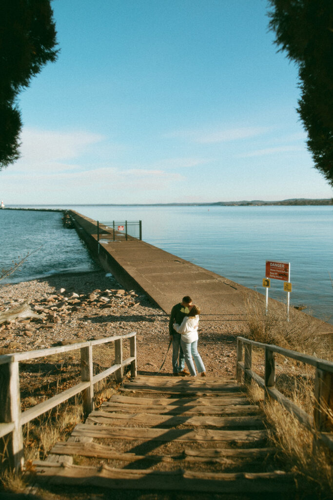 Couple kissing on the stairs at with Presque Isle Park behind them