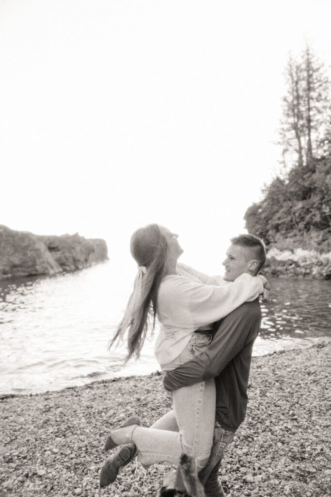 Black and white photo of a man picking up his fiancé for their Marquette Michigan engagement photos