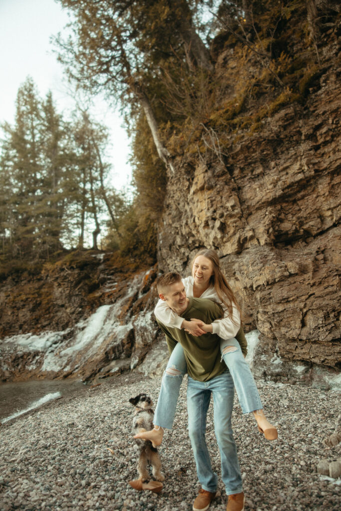 Man giving his fiancé a piggy back ride during their Marquette Michigan engagement photos