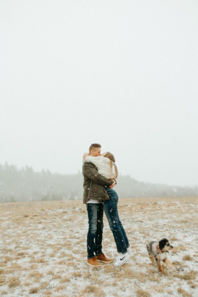 Couple kissing during their snowy engagement photos in an open field.