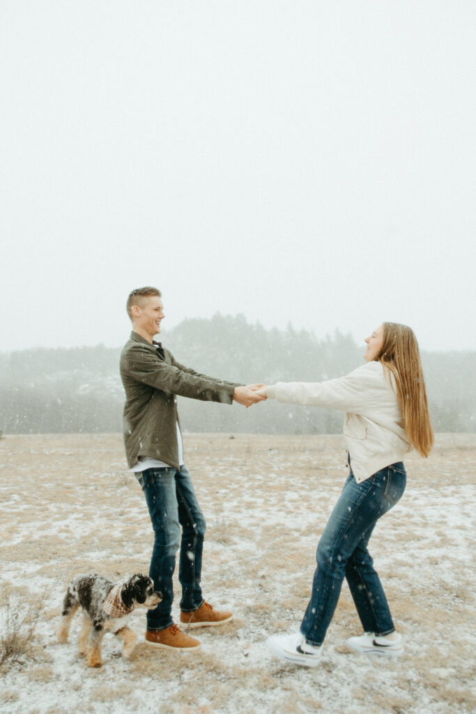 Couple being playful for their snowy Marquette Michigan engagement photos in an open field with their dog. 