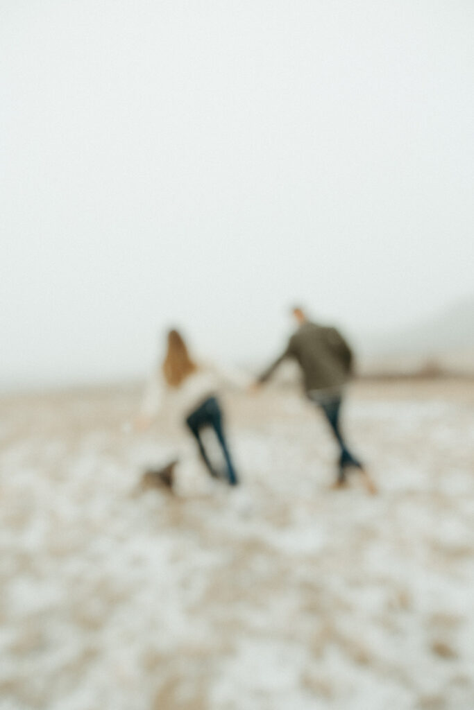 Man, woman and their dog running in an open field during their engagement session