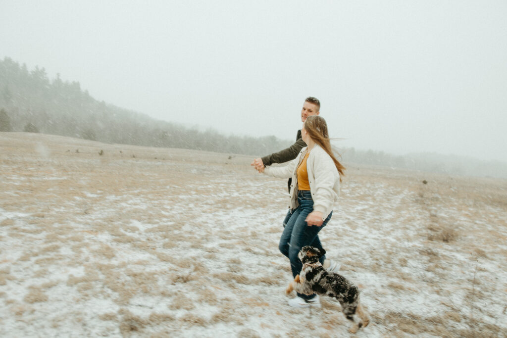 Man, woman and their dog running in an open field during their engagement session