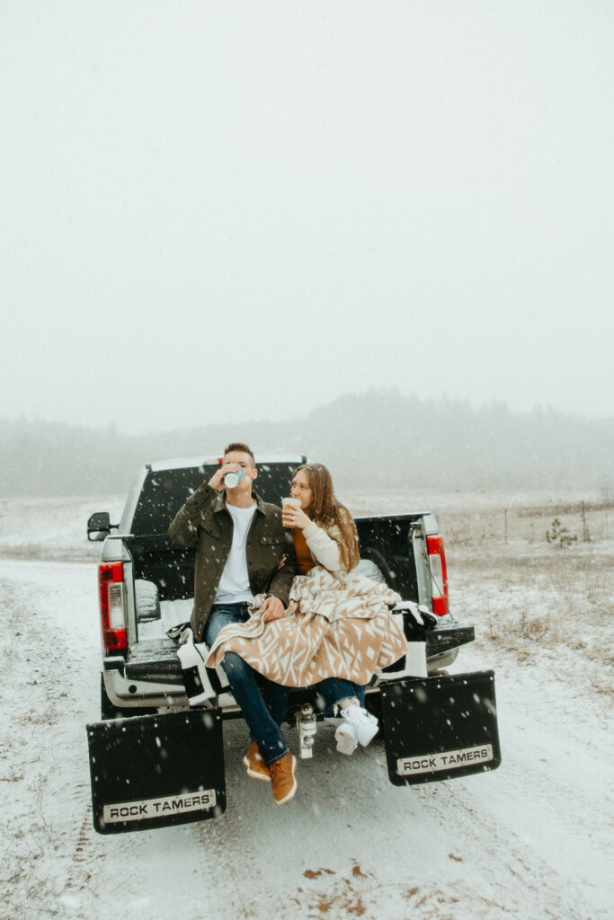 Couple sitting in the bed of a truck drinking coffee for their Marquette Michigan engagement photos