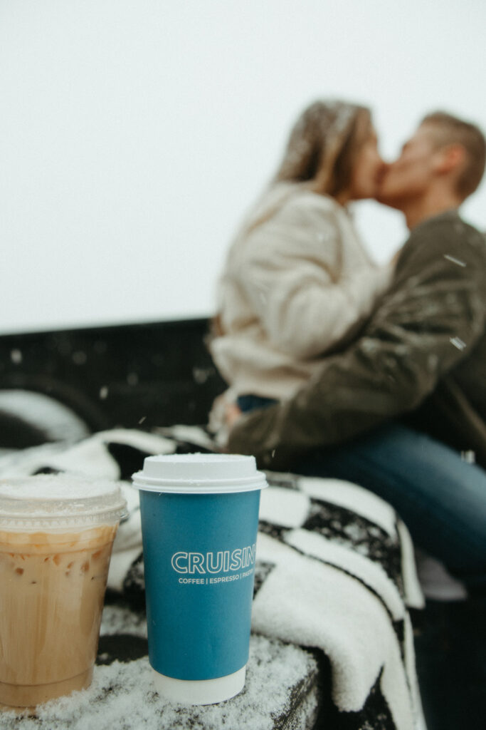Couple sitting on the bed of a truck for their Marquette Michigan engagement photos while it was snowing with coffee