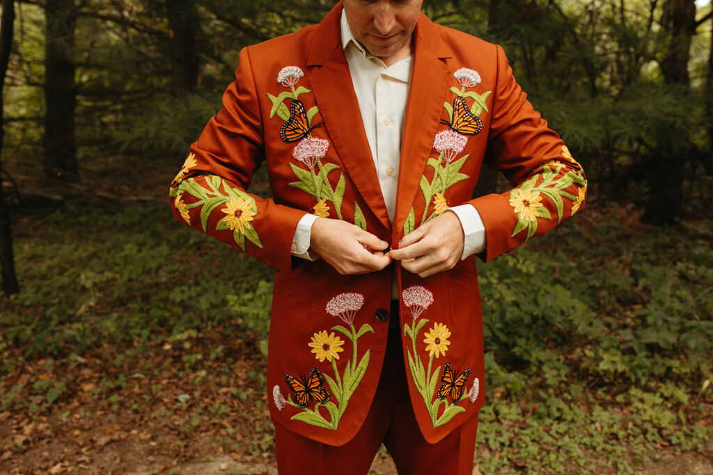 Groom wearing a red wedding suit with embroidered flowers and butterflies for a Greenhouse at Goldner Walsh wedding