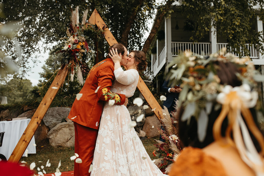 Bride and groom first kiss while guests throw flower petals