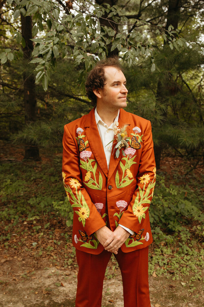 Groom wearing a red wedding suit with embroidered flowers and butterflies for a Greenhouse at Goldner Walsh wedding