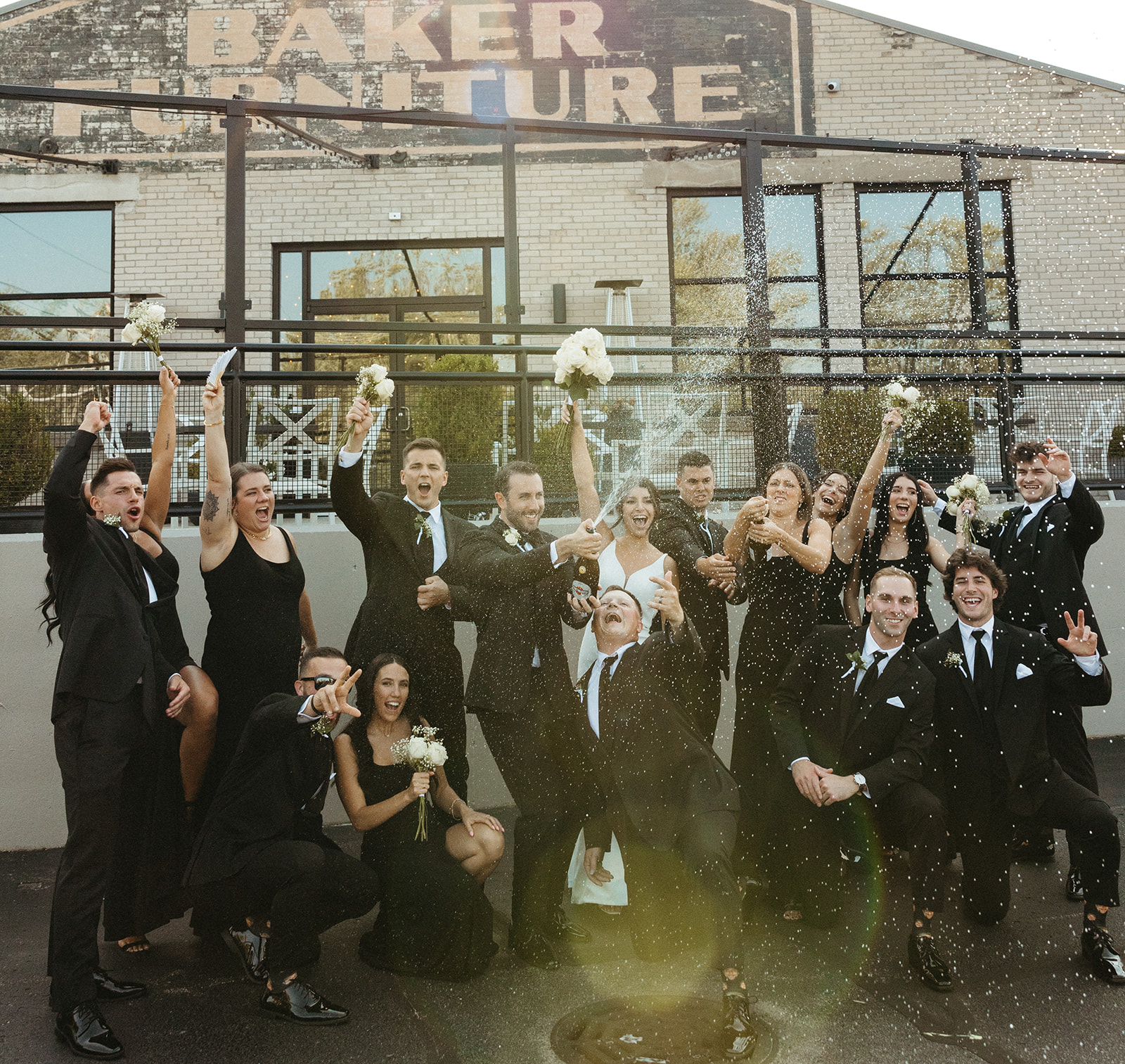 Bride, groom and their full wedding party popping champagne during their Baker Lofts Holland MI wedding reception. 