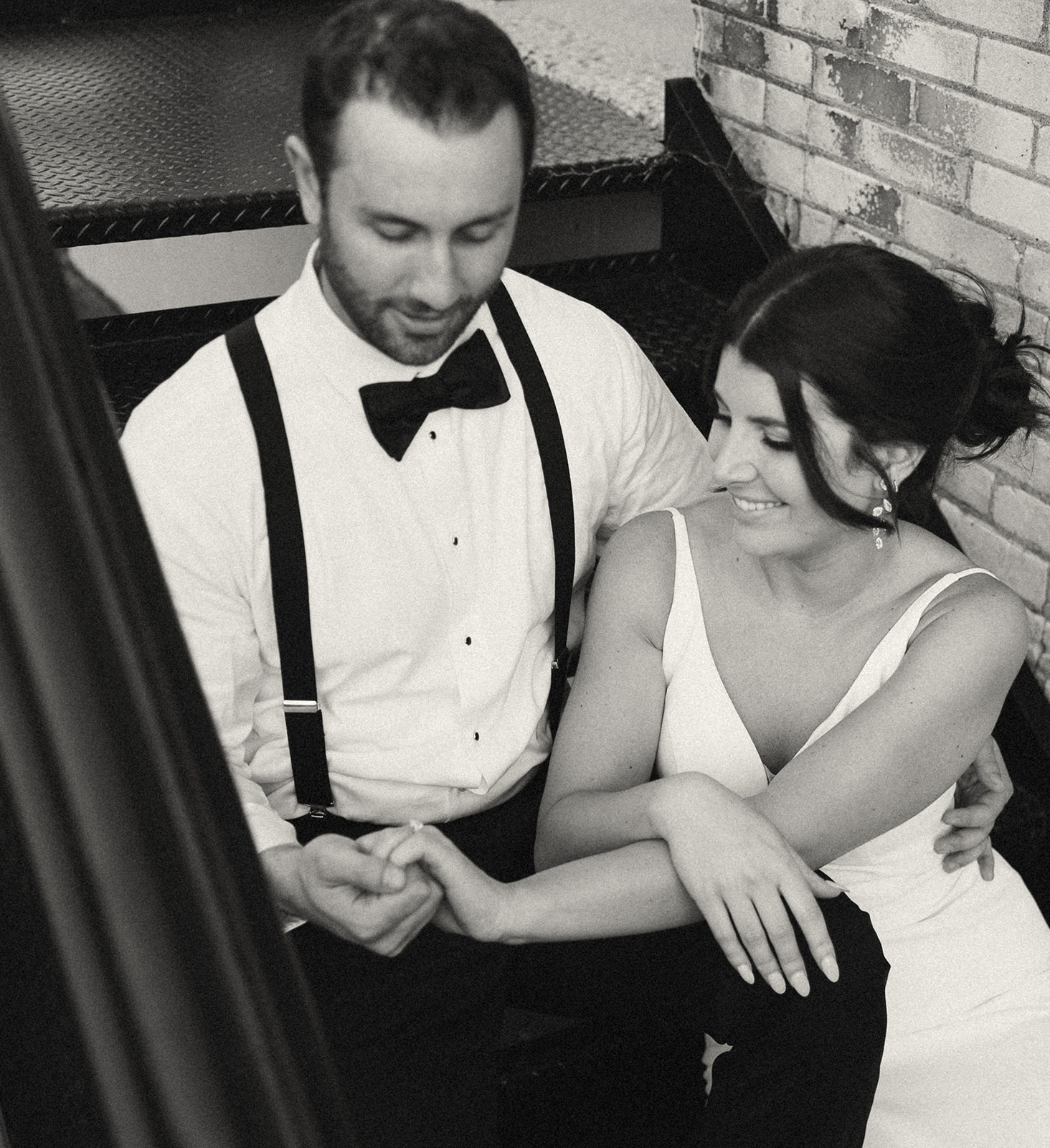 Black and white photo of a bride and groom sitting on stairs at Baker Lofts Holland MI wedding reception space