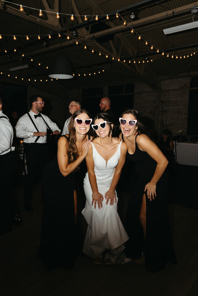 Bride and her bridesmaids wearing heart shaped sunglasses and posing for photos during the reception