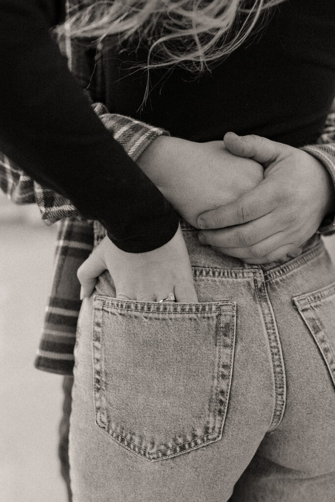 Black and white photo of a woman putting her hands in her back pocket to show off her engagement ring