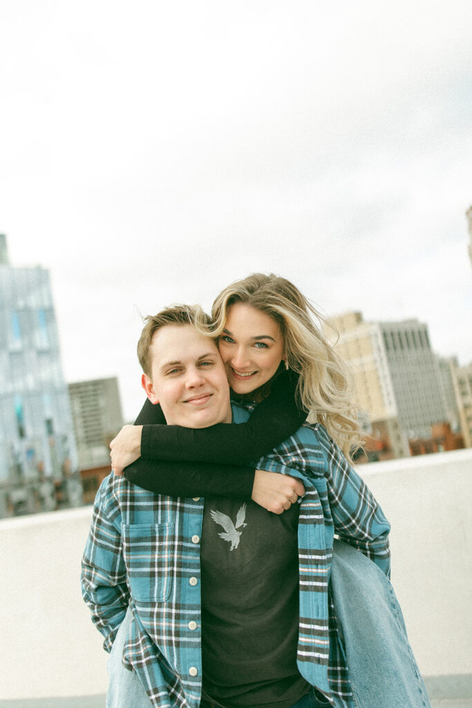 Man giving woman a piggy back ride during their downtown Detroit engagement photos on Z Lot