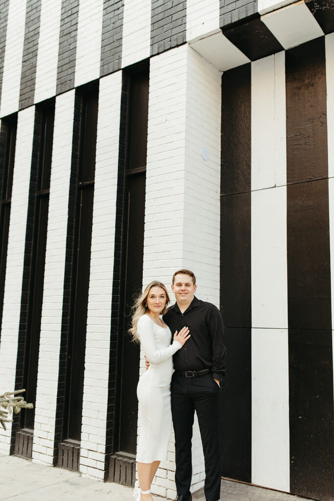Couple posing for their engagement session against a black and white striped wall