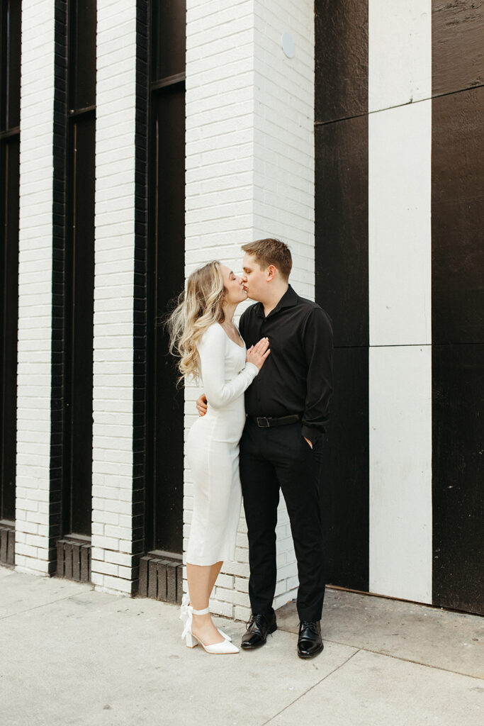 Black and white photo of a couple posing for their engagement session against a black and white striped wall