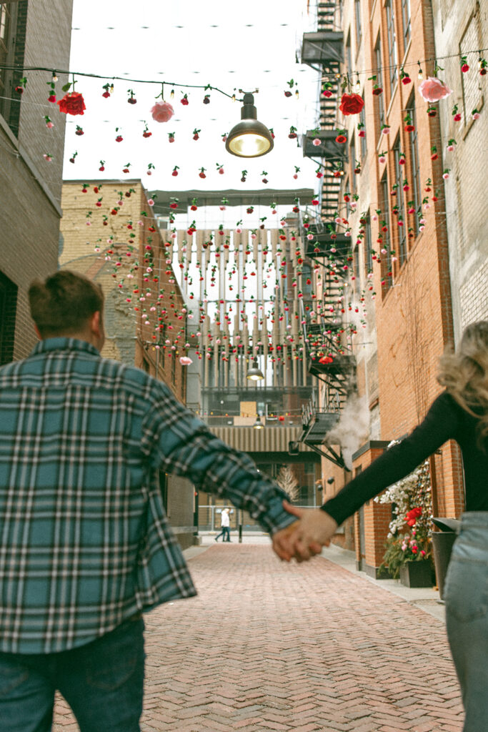 Couple holding hands as they walk down The Belt alleyway in downtown Detroit for their engagement photos