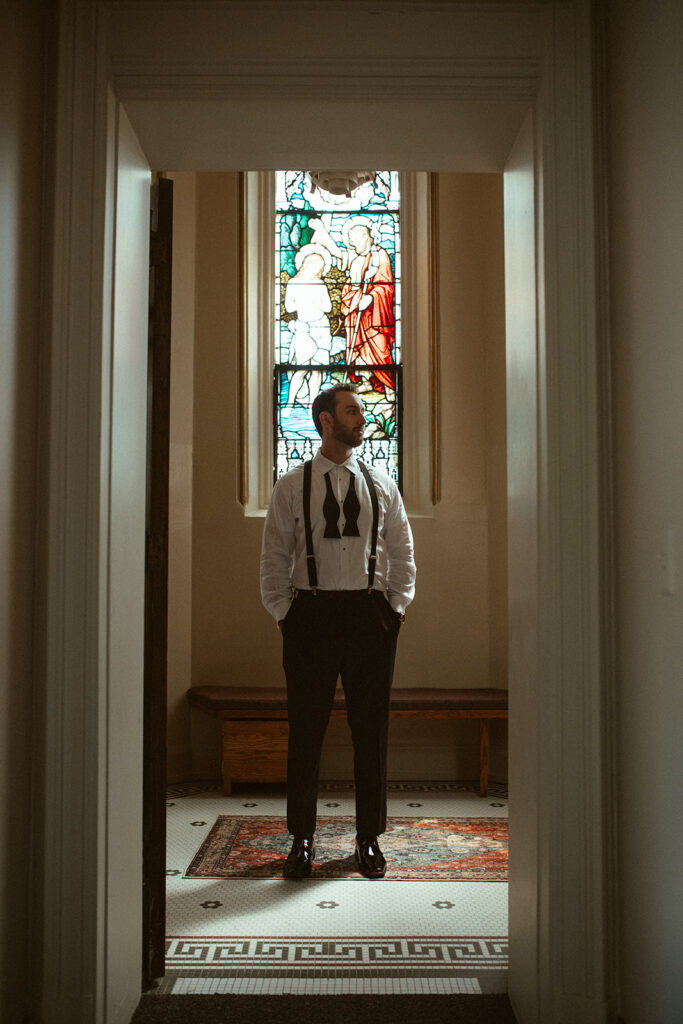 Groom standing in front of the church window as he gets ready for his Grand Rapids wedding