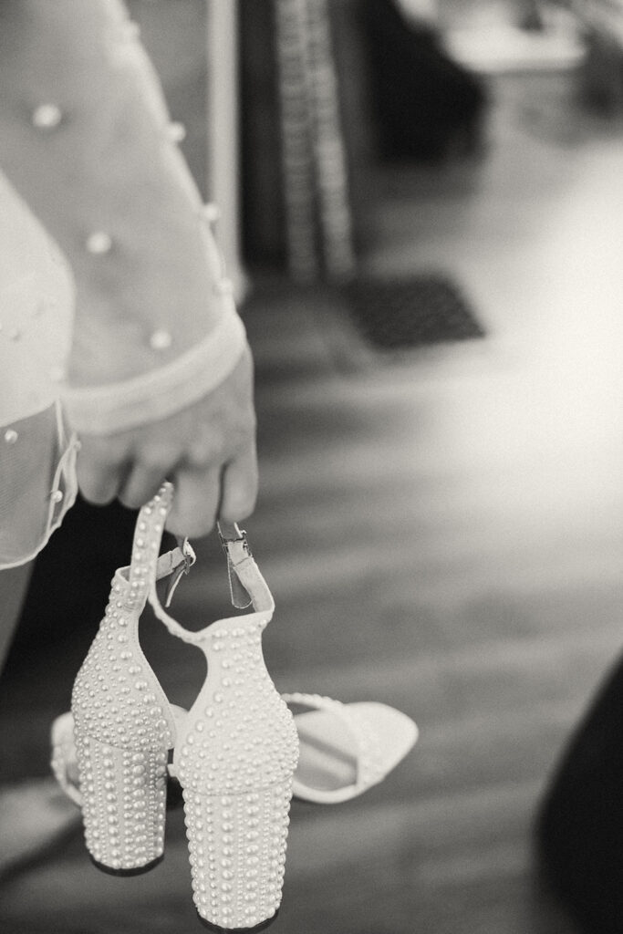 Black and white photo of a bride carrying her wedding heels