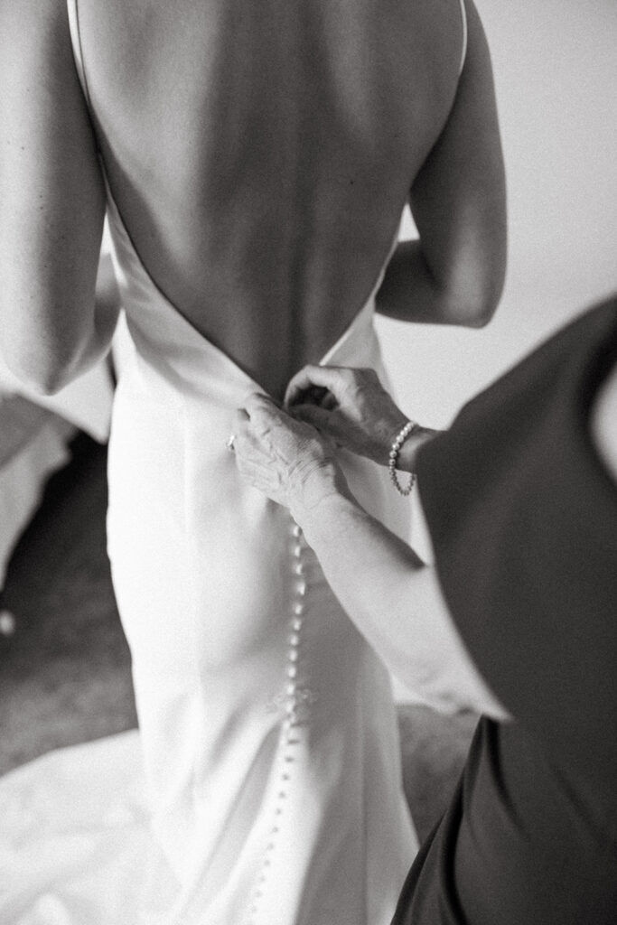 Black and white photo of a mother buttoning up her daughters wedding dress