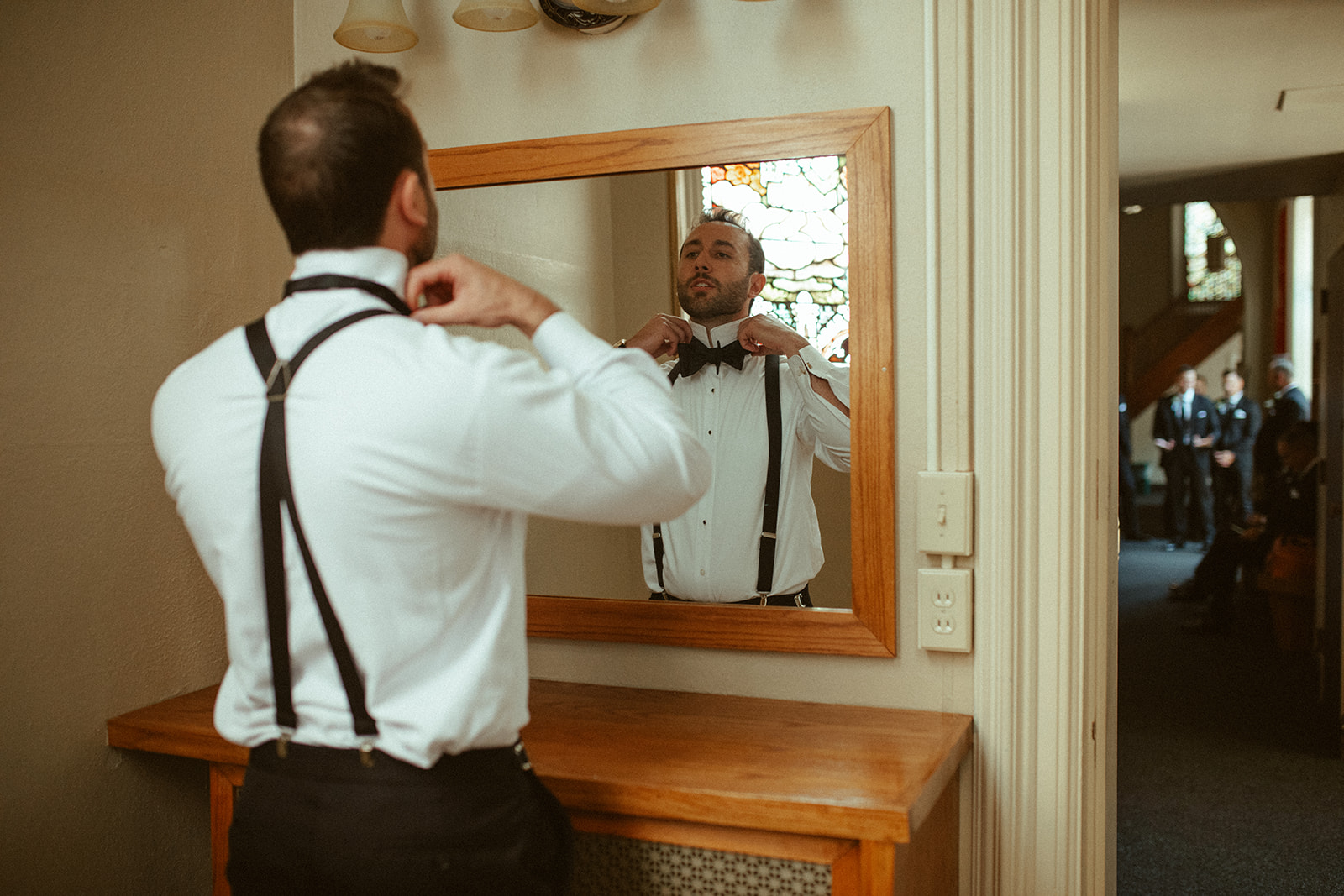 Groom looking at himself in the mirror as he gets ready for his Grand Rapids wedding with his groomsmen in the next room over