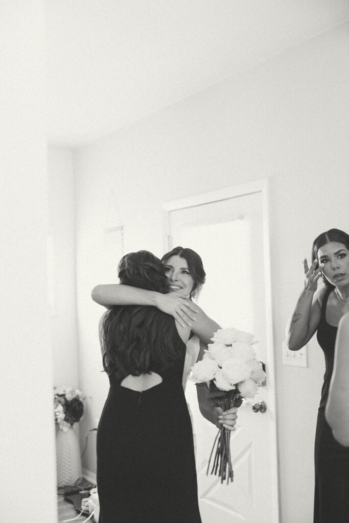 Black and white photo of a bride hugging her bridesmaids after an emotional first look