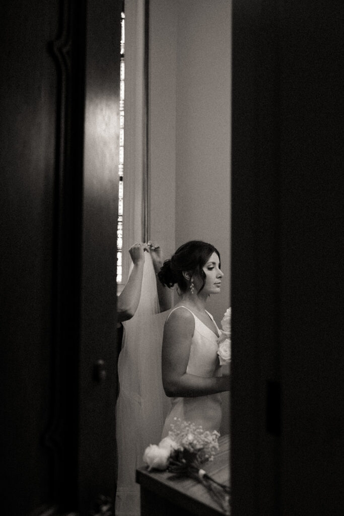 Black and white photo of a bride getting her veil put on