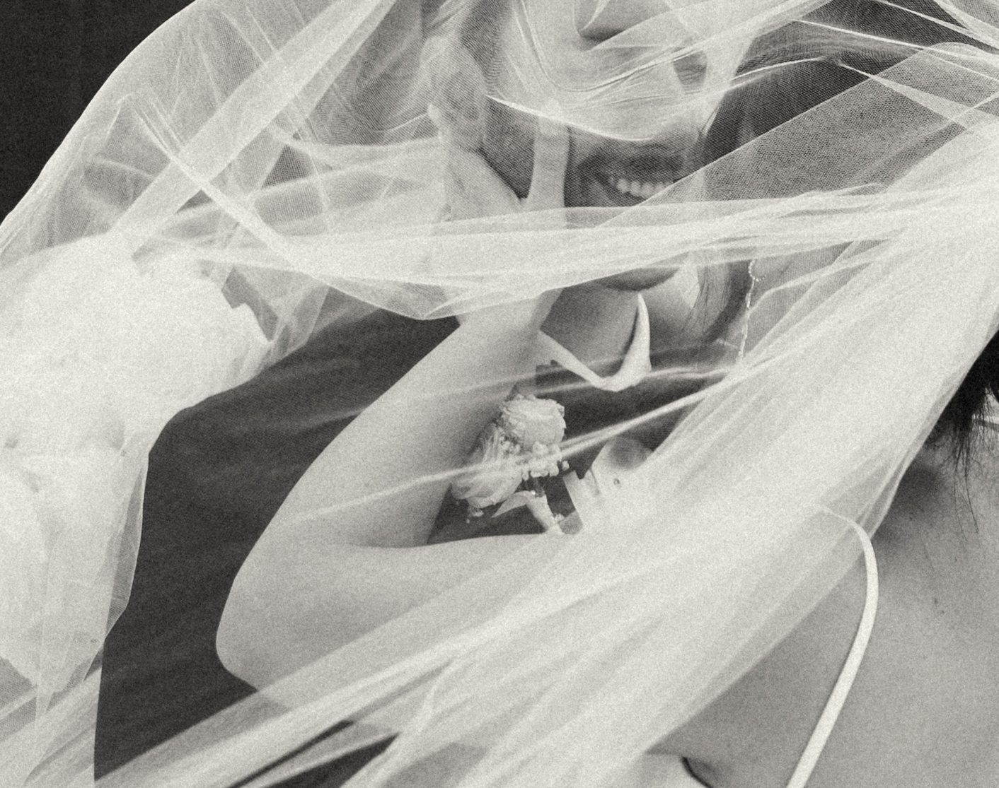 Black and white photo of a bride and groom posing for portraits underneath a wedding veil 