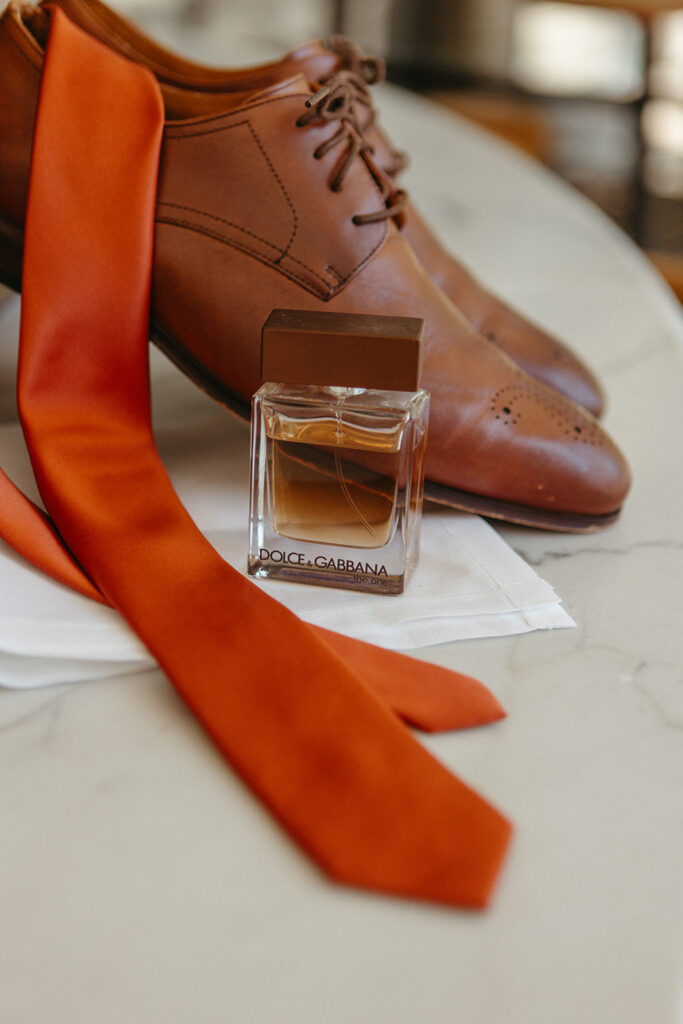 Grooms shoes, cologne, and orange tie