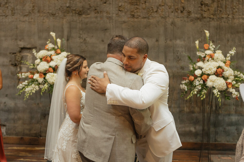 Groom hugging the father of the bride as he gives his daughter away at the altar at Jam Handy wedding venue