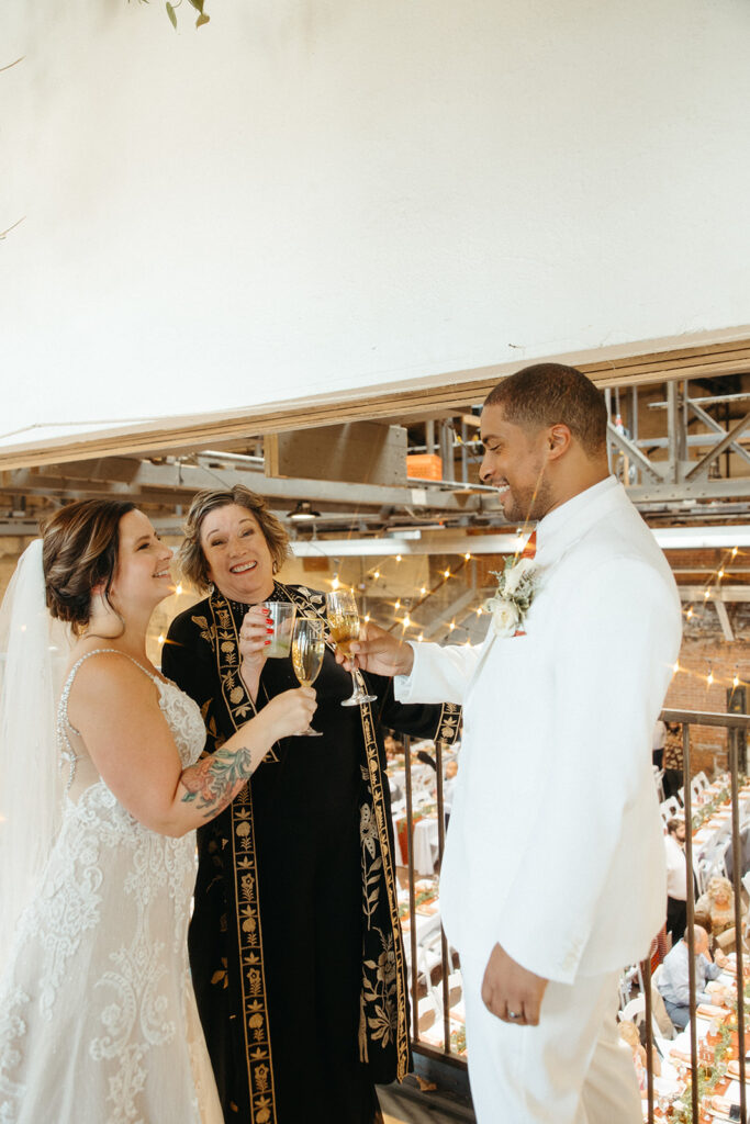 Bride, groom and their officiant toasting drinks