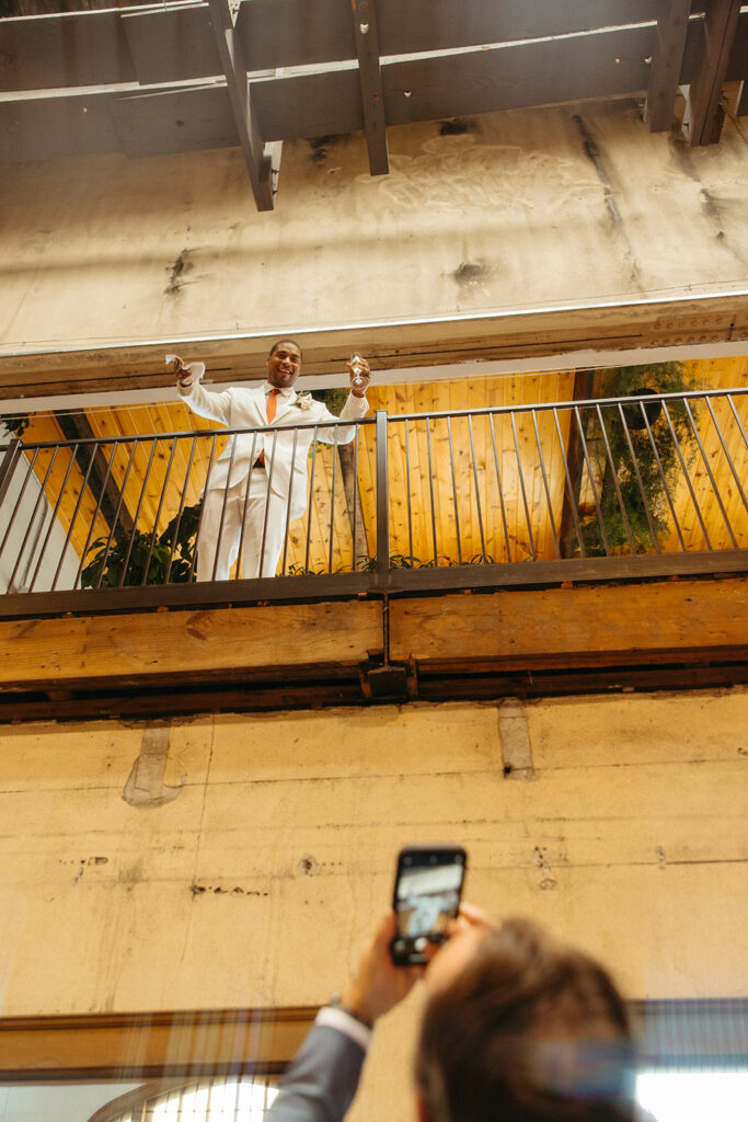 Guest taking a photo of a groom on a balcony