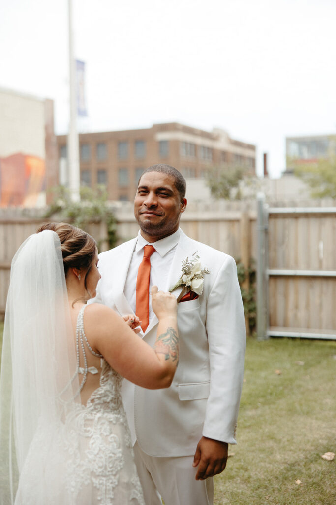 Bride putting a souvenir on grooms suit outside of Jam Handy wedding venue in Detroit, Michigan