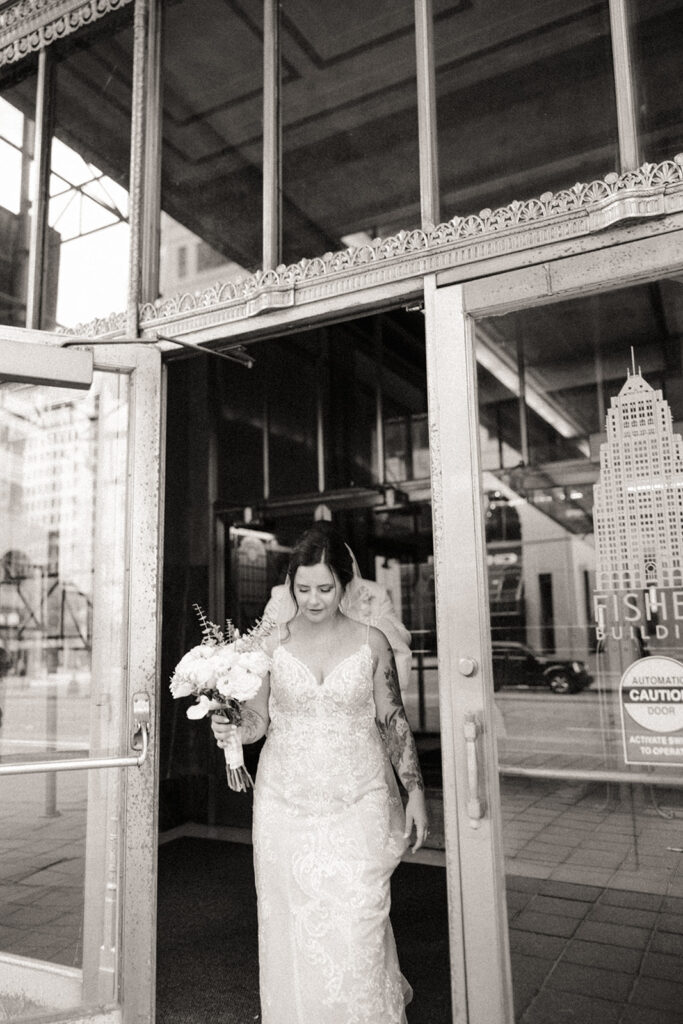 Black and white photo of a bride and groom walking out of Fisher Building in Detroit
