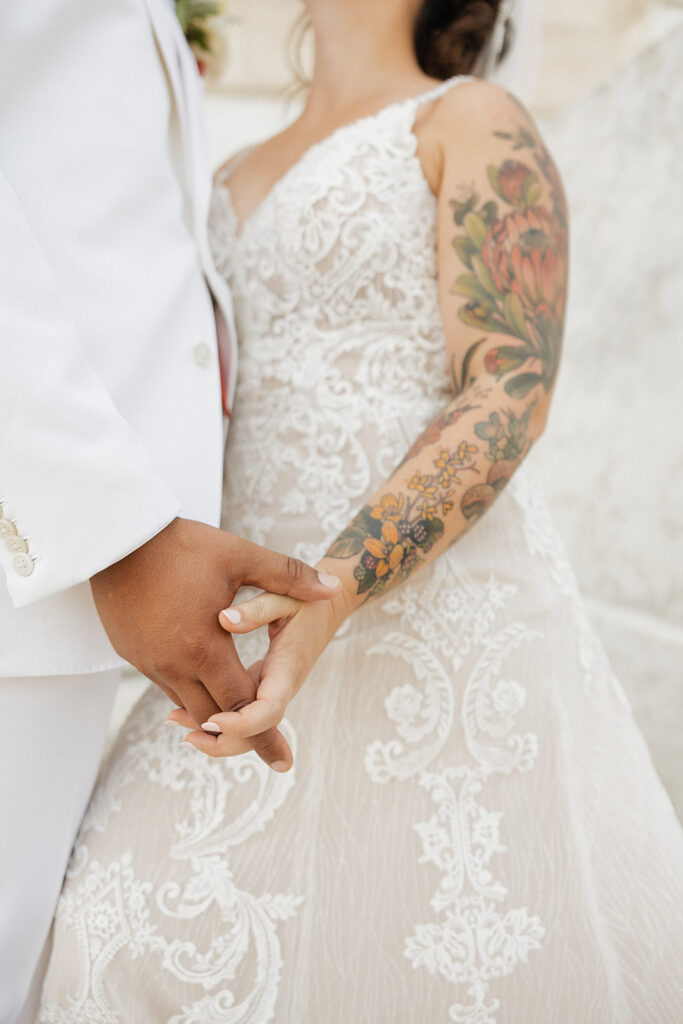Close up of a tattooed bride and her groom holdings hands