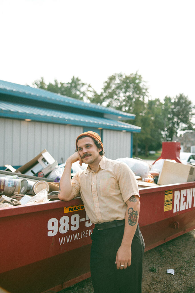 Man leaning against a large dumpster outside