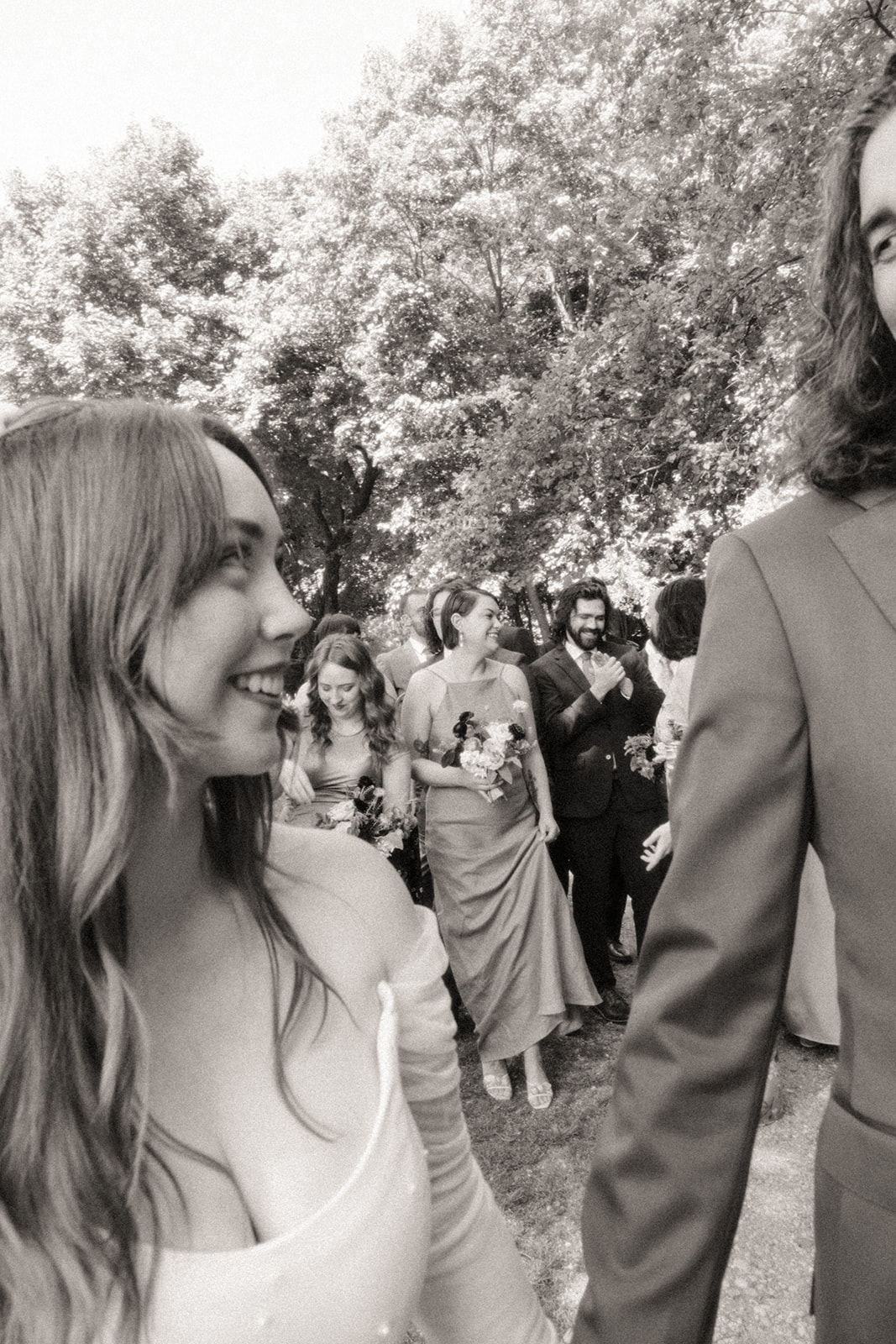 Black and white candid wedding photo of a bride and groom walking with their wedding party at Stony Creek Metropark in Detroit, Michigan