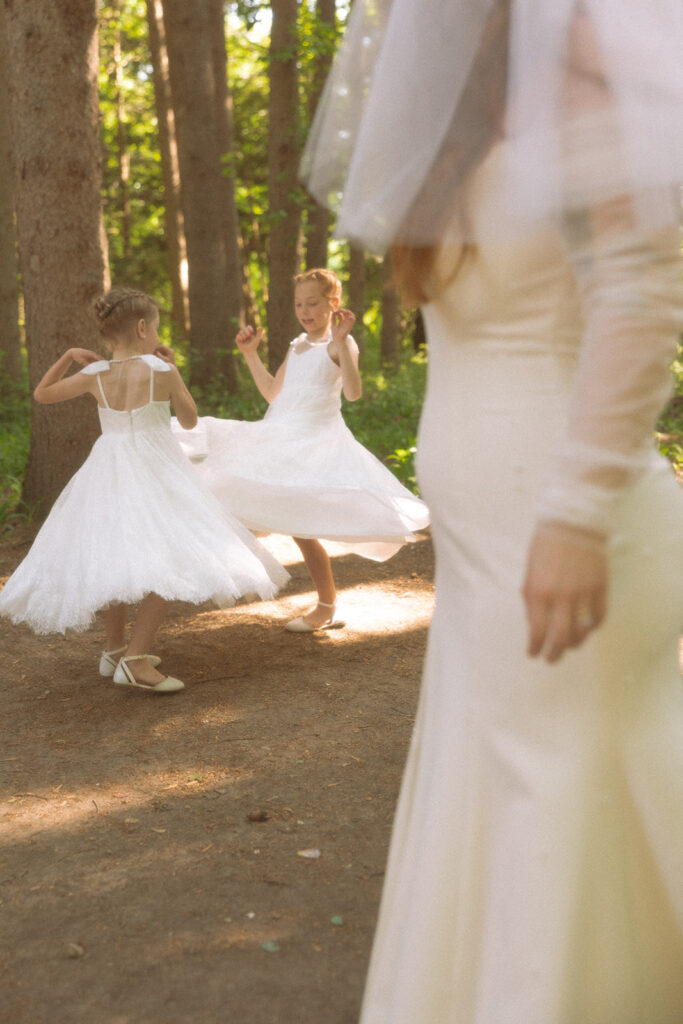 Bride watching her flower girls play in the woods