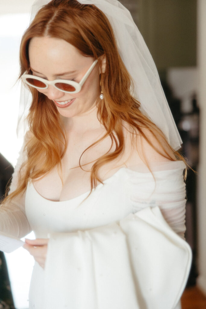 Bride wearing a whimsy fitted white dress, long veil, and round sunglasses 