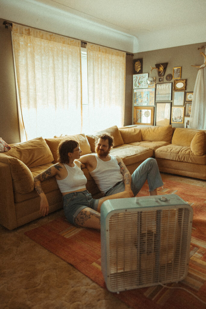 Couple sitting on their living room floor with a box fan for their at-home couples photoshoot