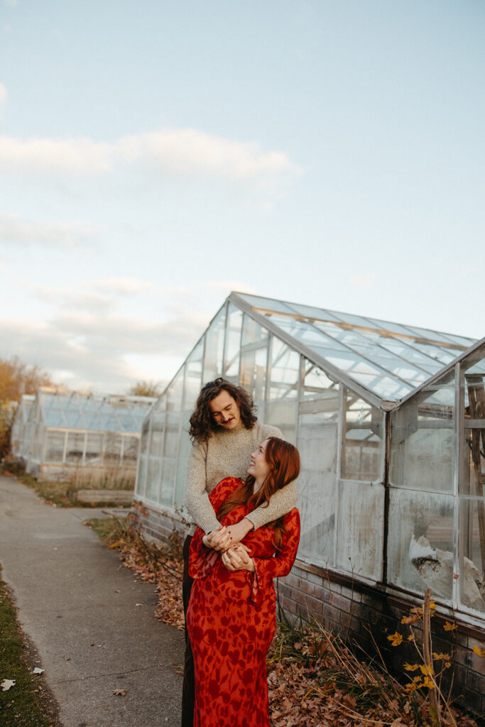 Man and woman posing in front of a Greenhouse for their Belle Isle engagement photos in Detroit, Michigan