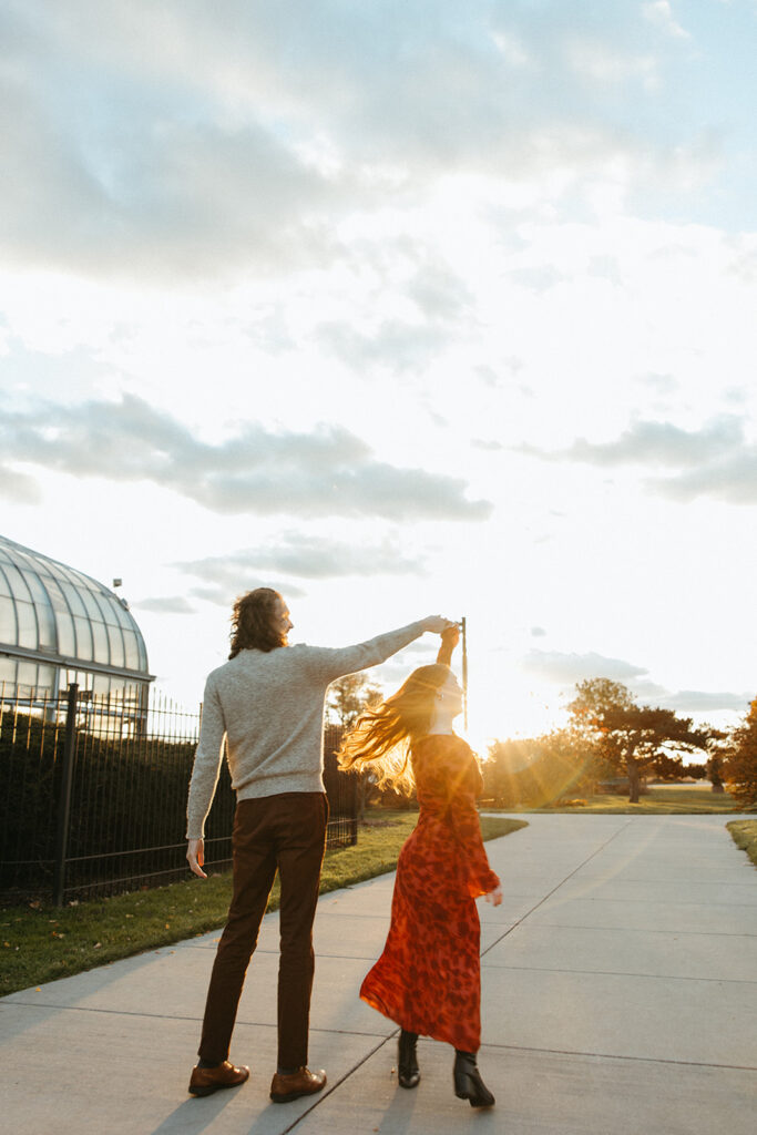 Man twirling his fiancé during during their fall sunset Belle Isle engagement photos in Detroit, Michigan