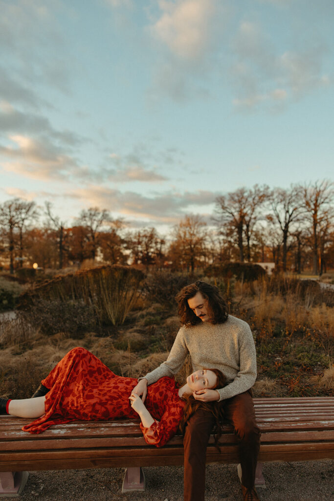 Woman laying with her head on her fiancés lap on a park bench during their Belle Isle engagement photos in Detroit, Michigan