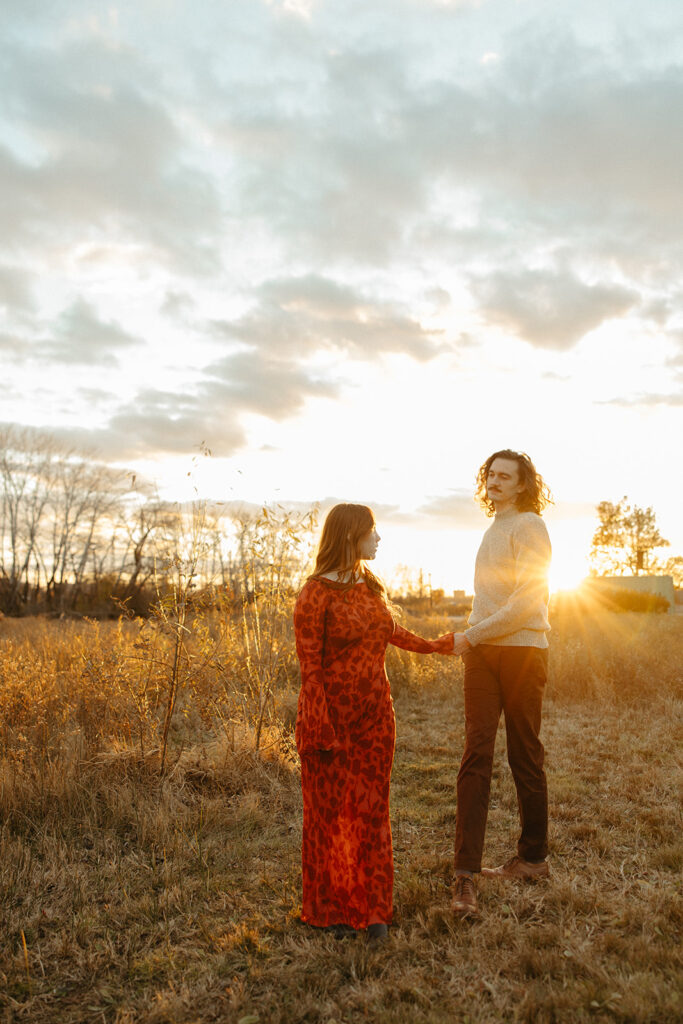 Couple posing in an open field at sunset during their fall Belle Isle engagement photos in Detroit, Michigan