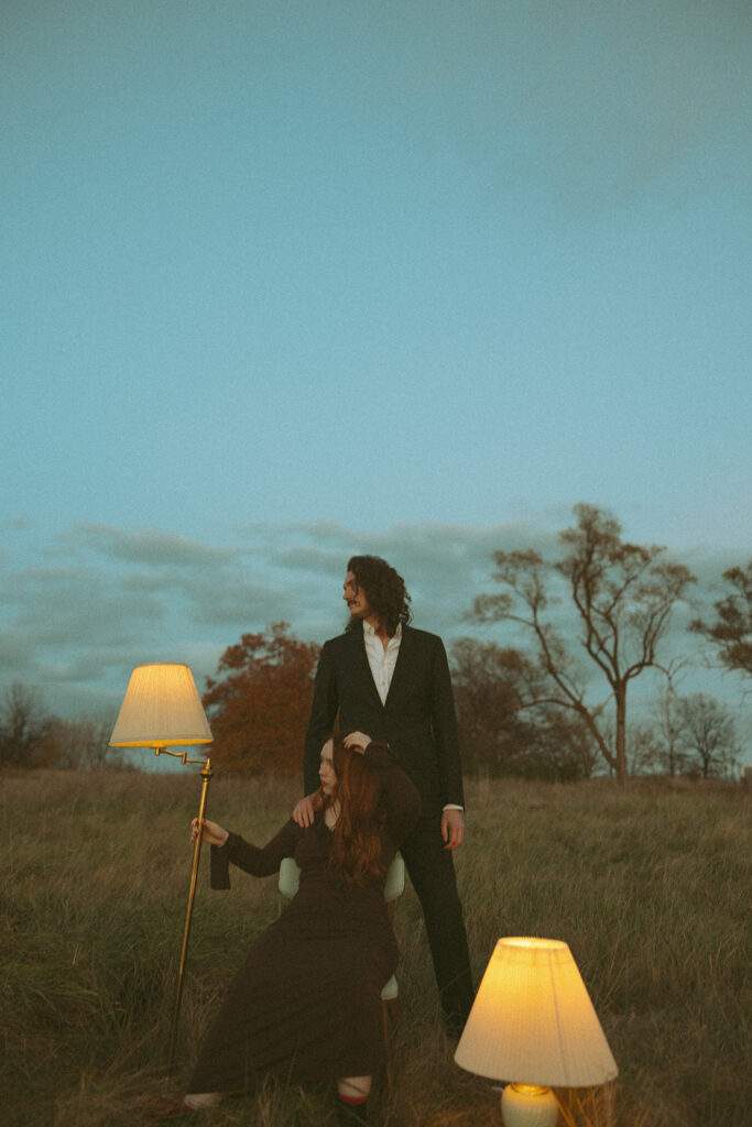 Couple sitting in an open field with lampshades posing for photos