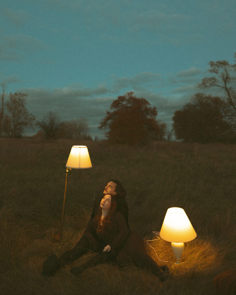 Couple sitting in an open field with lamp shades during their fall engagement shoot in Michigan